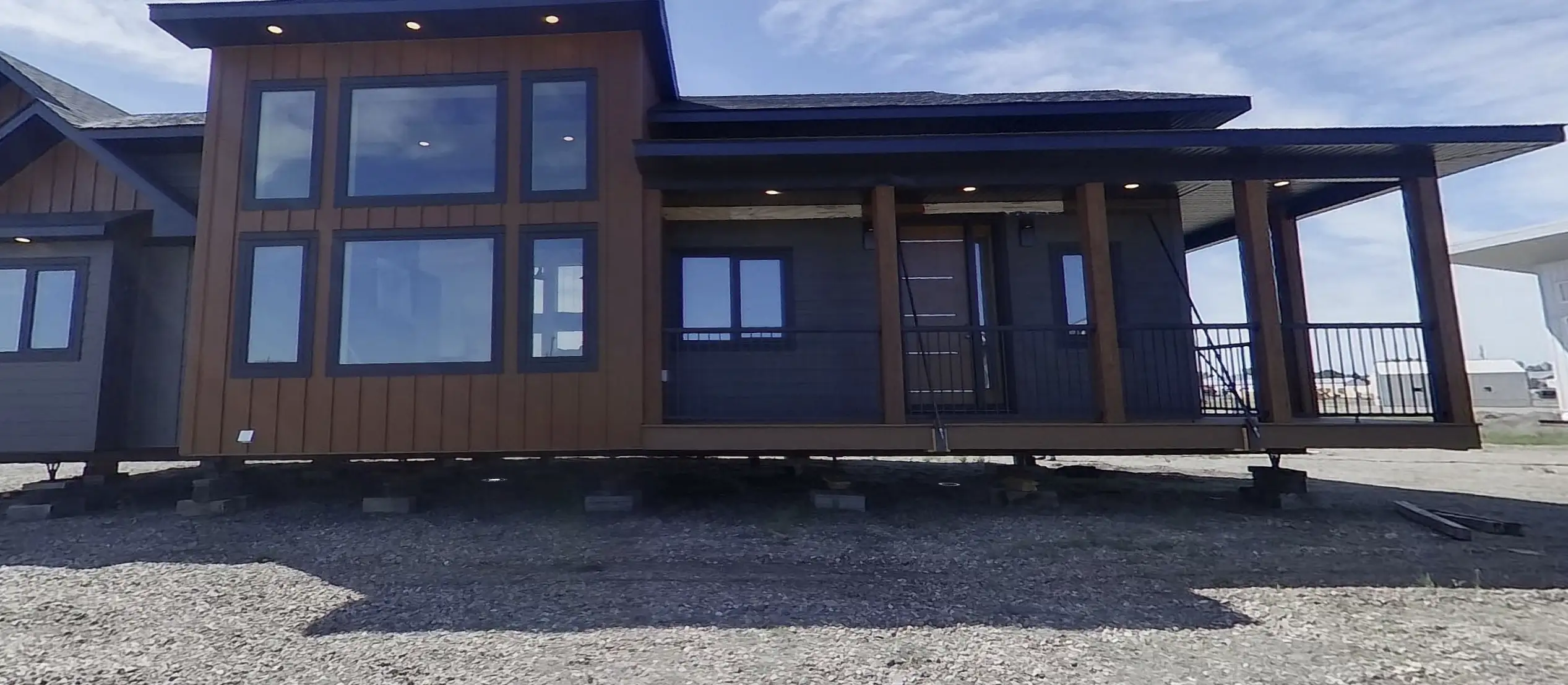 Modern RTM home exterior in Alberta or Saskatchewan with tall black framed windows and a covered front porch, shown elevated on blocks ready to move.
